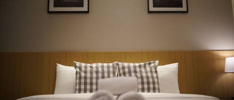 A neatly made bed with rolled towels, a wooden headboard, and two framed pictures on the wall.