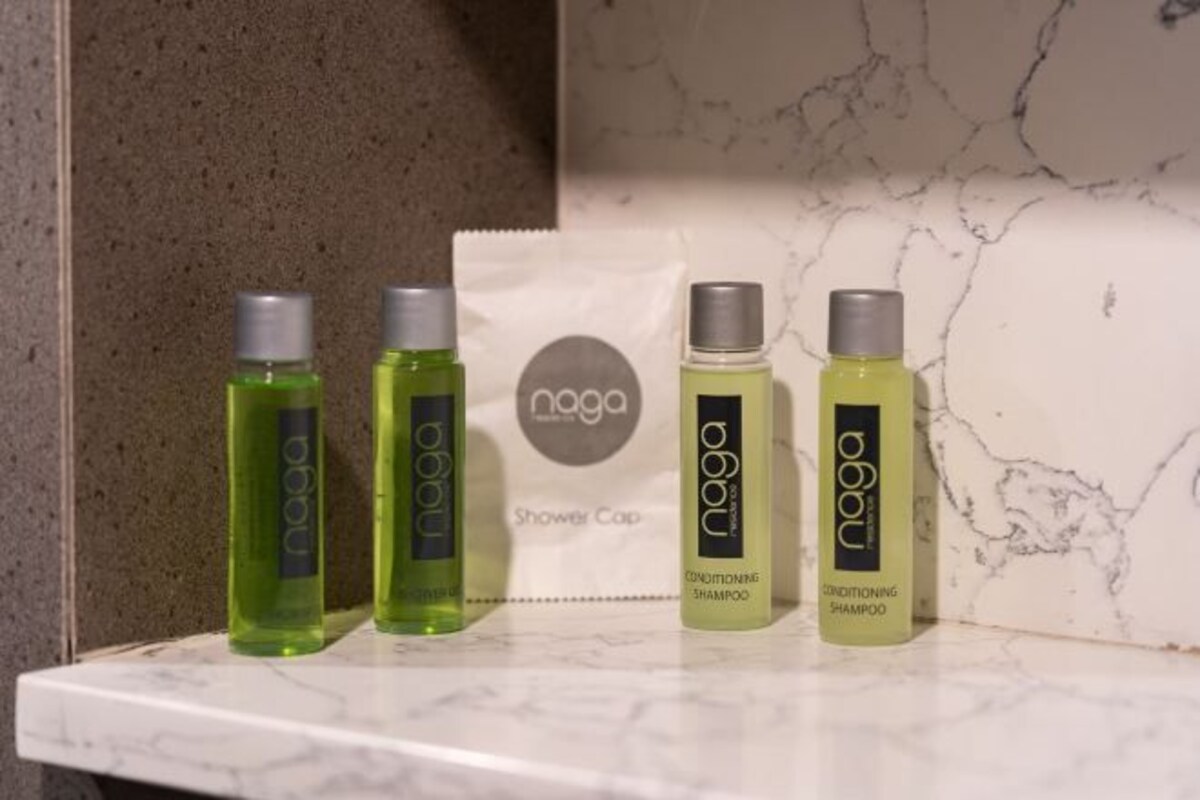 A bathroom shelf with four bottles of Naga shower cap and conditioner shampoo.