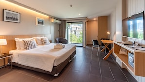 A modern hotel room with a large bed, a desk with a computer, a TV, and a balcony with a city view. - Naga Residence (Bangkok)