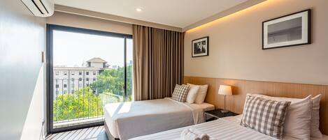 A hotel room with two beds, a large window with curtains, a wall-mounted air conditioner, and a framed picture.