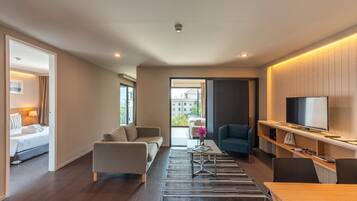 Una habitación de hotel moderna con cama, sofá, mesa de centro, televisor y un balcón con vistas.