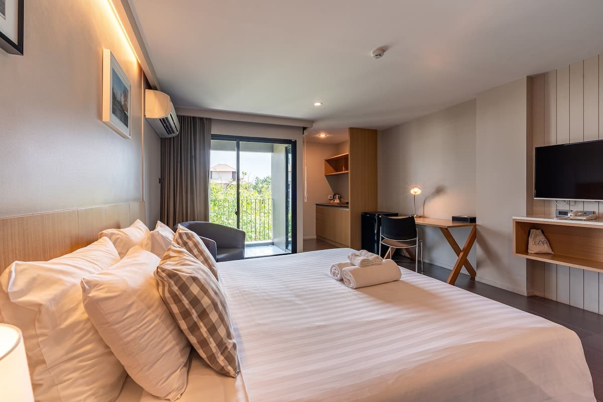 A hotel room with a large bed, a desk, a TV, and a balcony with a view.