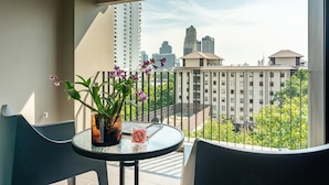A balcony with a table and chairs, a potted orchid, and a view of city buildings. - Naga Residence (Bangkok)