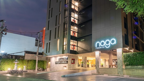 A modern hotel with a prominent 'naga' sign, a well-lit entrance, and a landscaped area with a fountain. - Naga Residence (Bangkok)