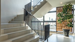 A modern staircase with a black railing, leading to a landing with a large potted plant. - Naga Residence (Bangkok)