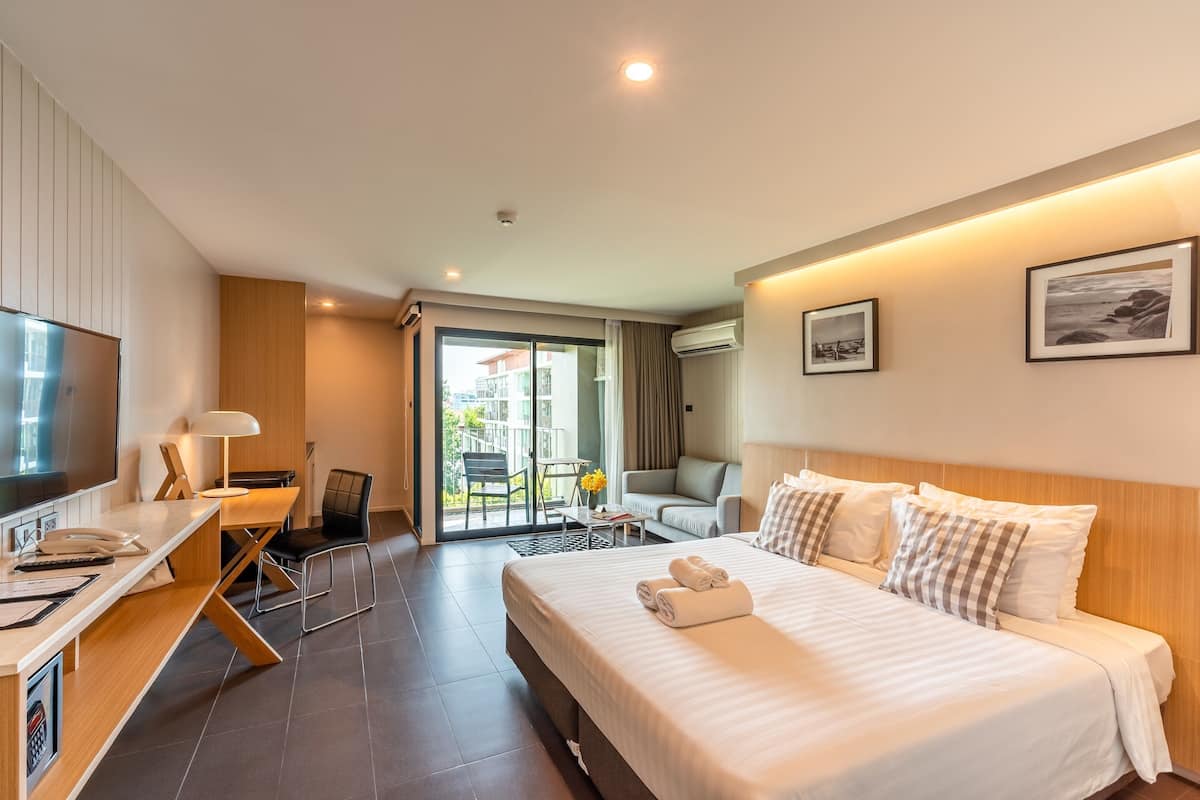 A hotel room with a bed, a desk with a computer, a chair, a TV, and a balcony with a view.