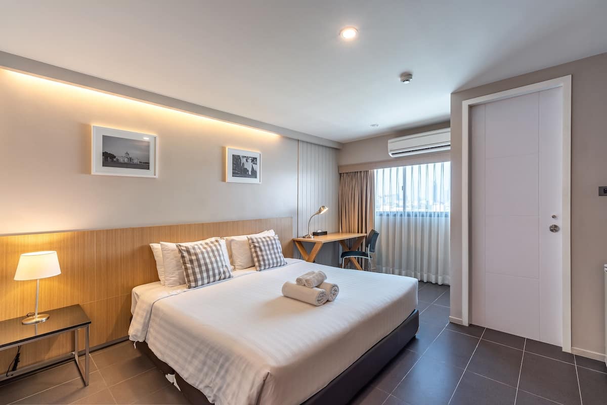 A modern hotel room with a neatly made bed, a desk, and two framed pictures on the wall.