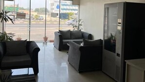 A reception area with a large window, a seating area with sofas, and a refrigerator. - Binayat Hama Serviced Apartments (Al Jubail)