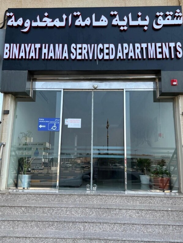 L’entrée d’un immeuble avec une enseigne indiquant « Binayat Hama Serviced Apartments ».