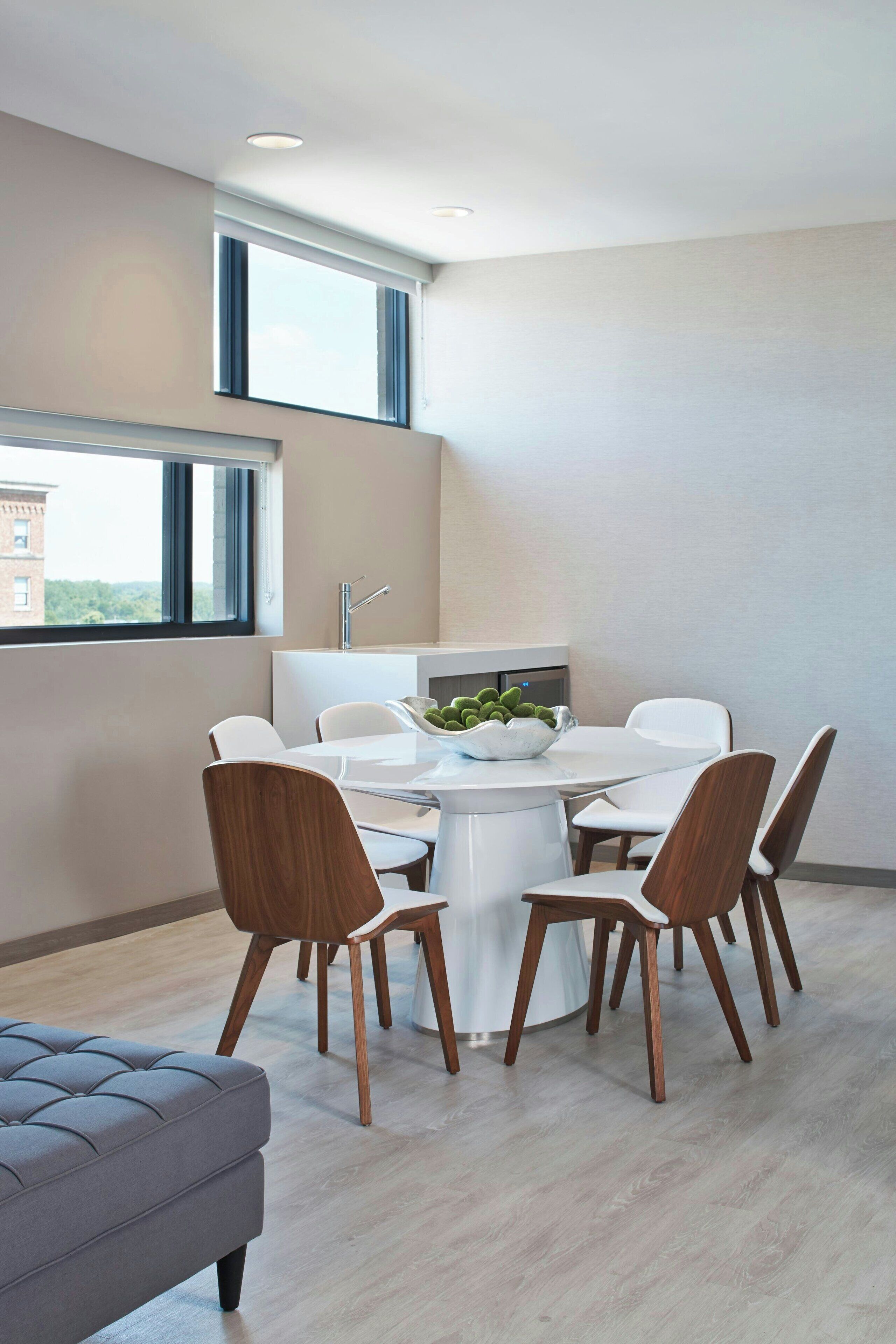 A modern dining area with a round table, white chairs, and a bowl of fruit.