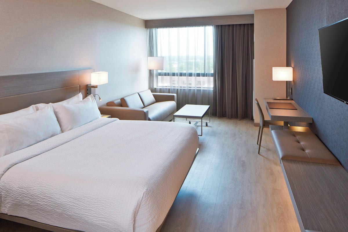 Una habitación de hotel con una cama grande, un sofá, una mesita y un televisor.