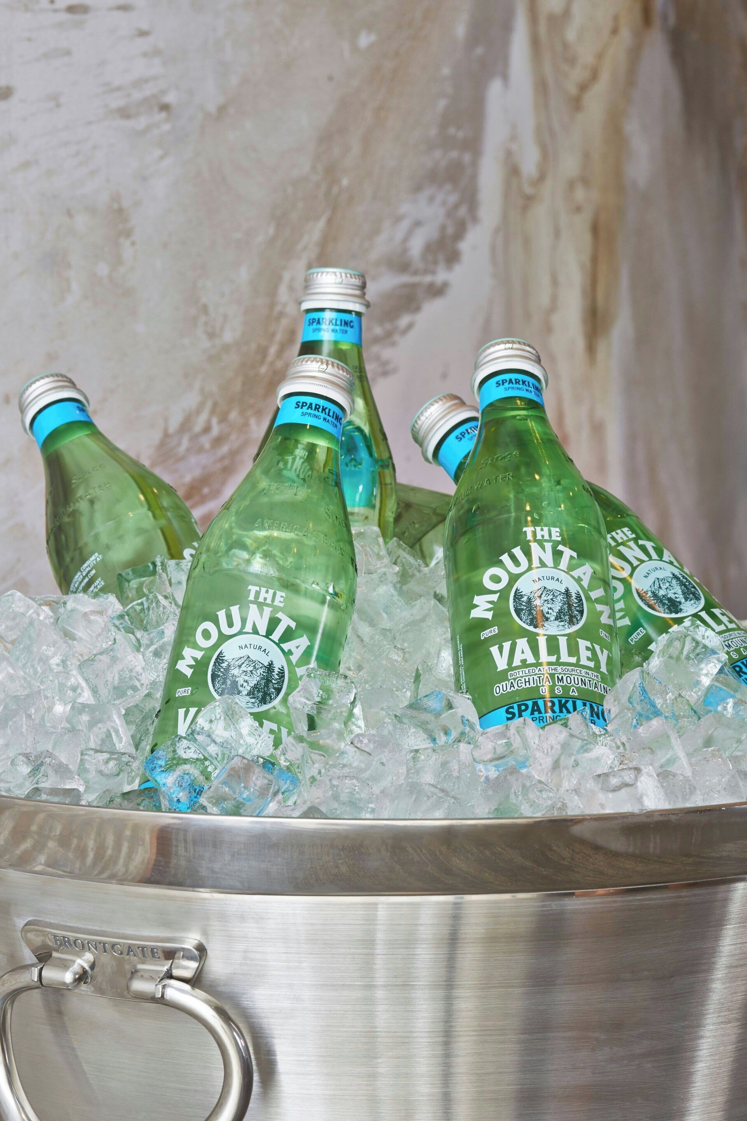 Une glacière en acier inoxydable remplie de glace et contenant plusieurs bouteilles d’eau pétillante Mountain Valley.