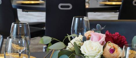 A dining table set with wine glasses, a candle, and a metal bucket with flowers.