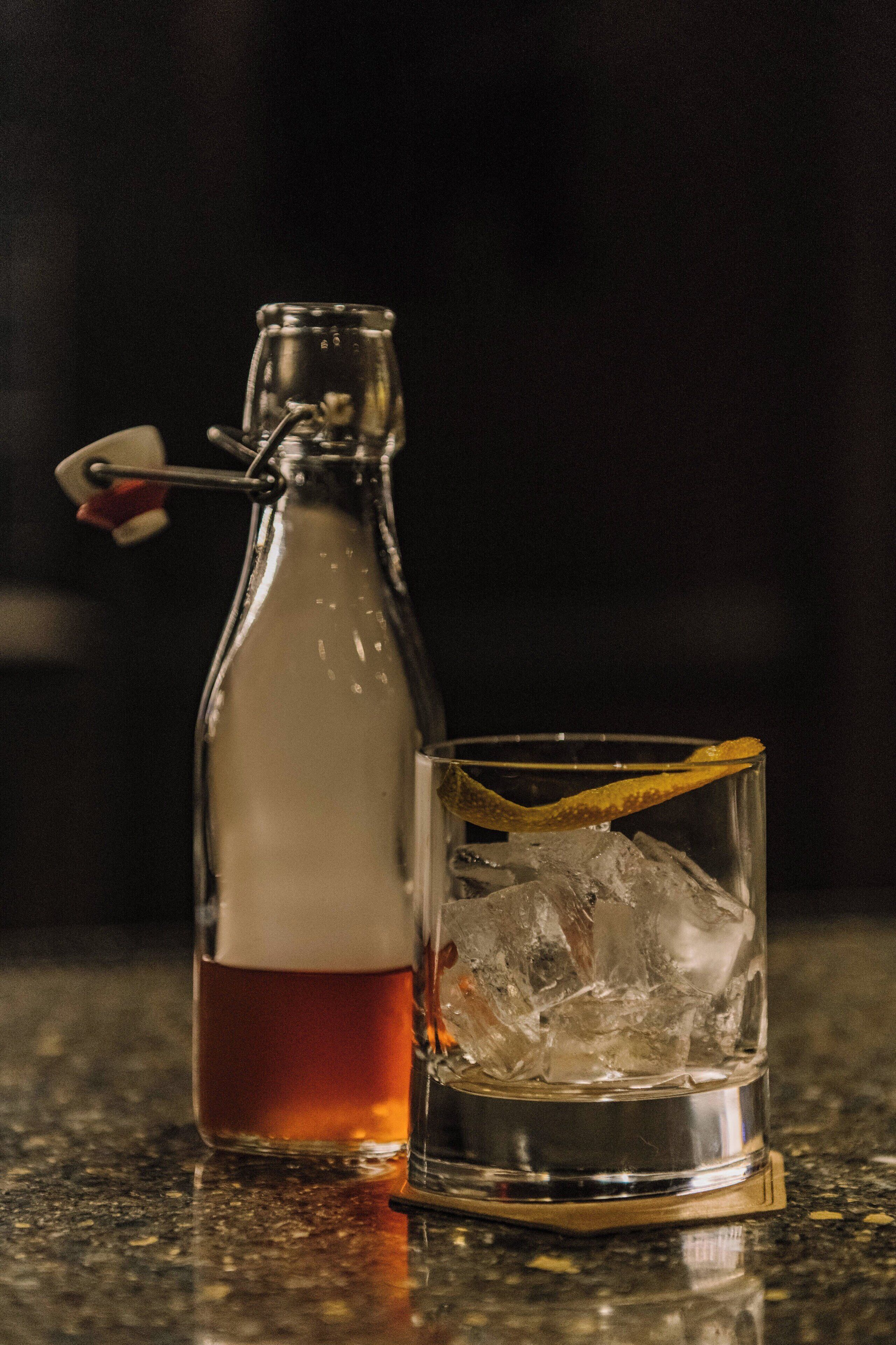 Una botella de líquido ámbar junto a un vaso con cubitos de hielo.