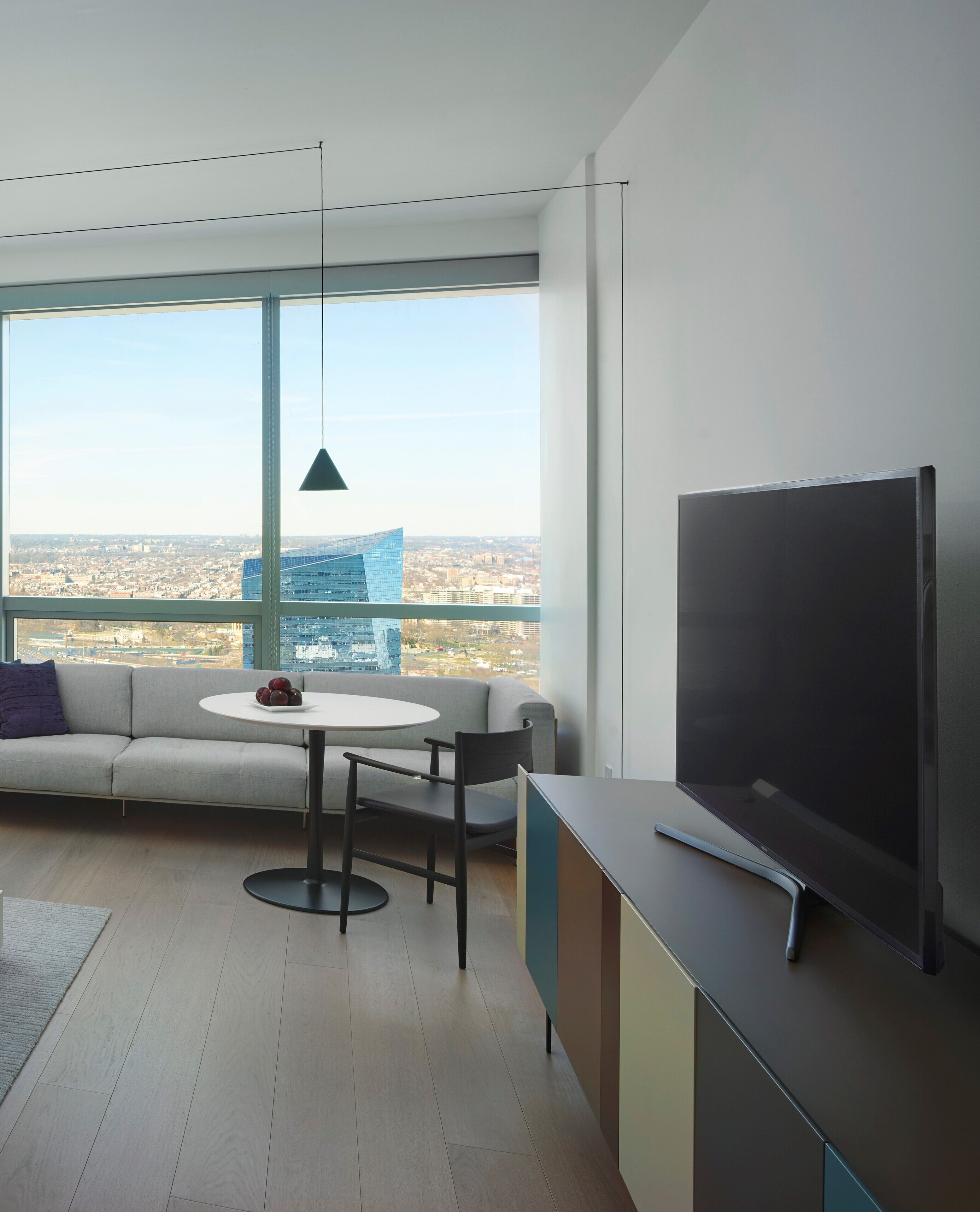 Una sala de estar moderna con un gran ventanal, un televisor de pantalla plana, un sofá, una mesita redonda y una lámpara colgante.