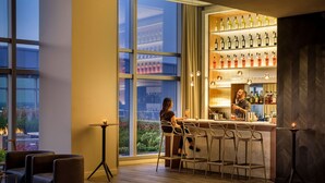 A modern bar area with a bartender, a woman seated at a table, and a large window offering a city view. - AKA University City (Philadelphia)