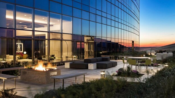 A modern building with a glass facade, outdoor seating area with a fire feature, and a view of the sunset. - AKA University City (Philadelphia)