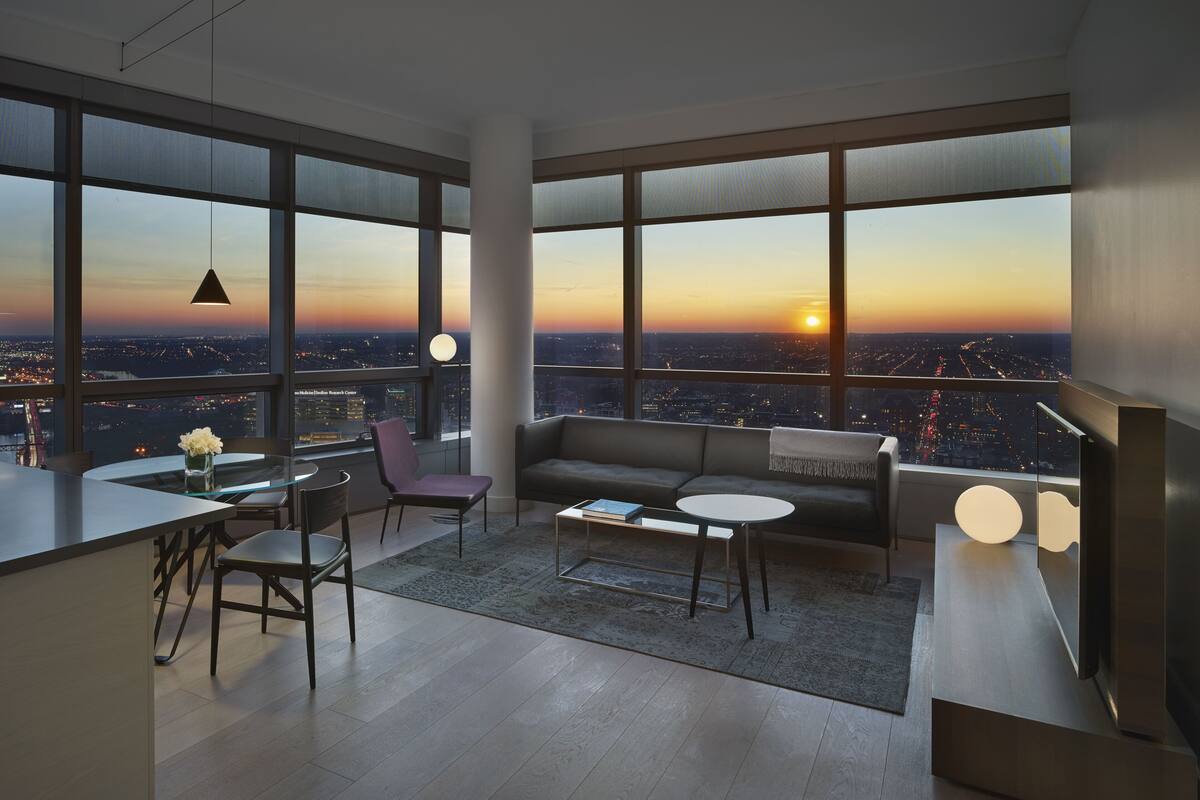 Un salon moderne doté de grandes fenêtres, d’un canapé, d’une table basse et d’un coin repas avec une table et des chaises.