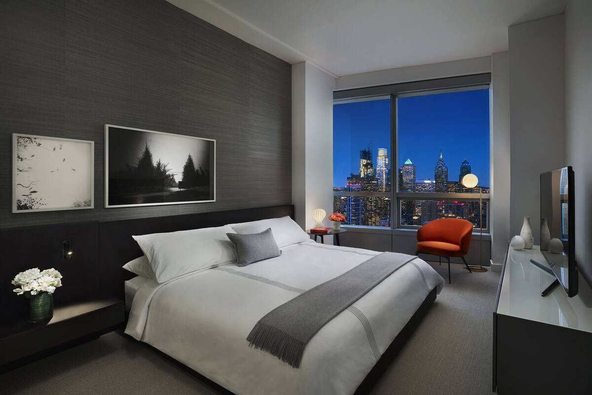 Une chambre d’hôtel moderne, dotée d’un grand lit, d’un bureau et offrant une vue sur les lumières de la ville la nuit.