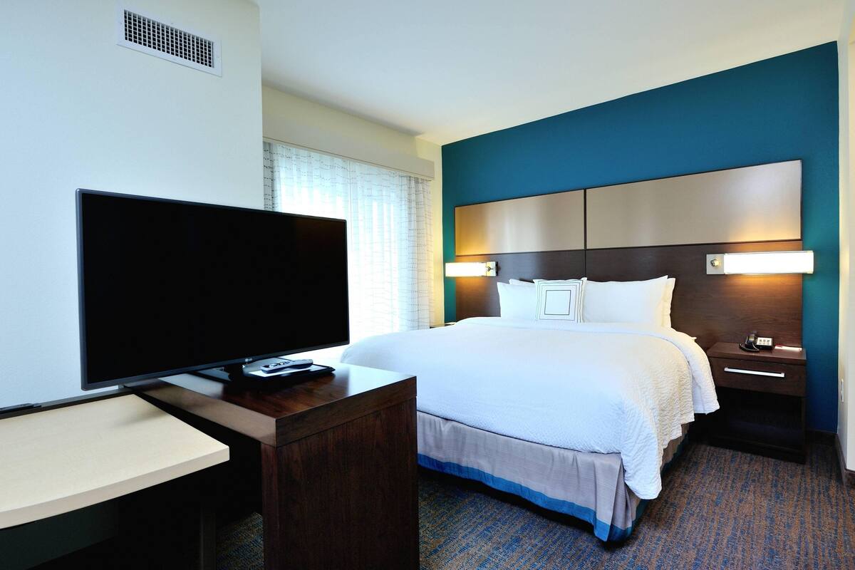 A hotel room with a bed, bedside table, TV, and a desk with a chair.
