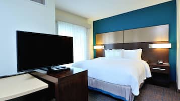 A hotel room with a bed, bedside table, TV, and a desk with a chair.