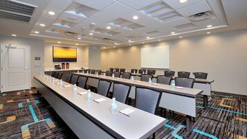 A conference room with a long table, chairs, water bottles, and a projector screen.
