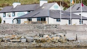 A coastal building with multiple windows and a stone wall in front. - The Beach Day's Bar & B&B (Inishbofin)
