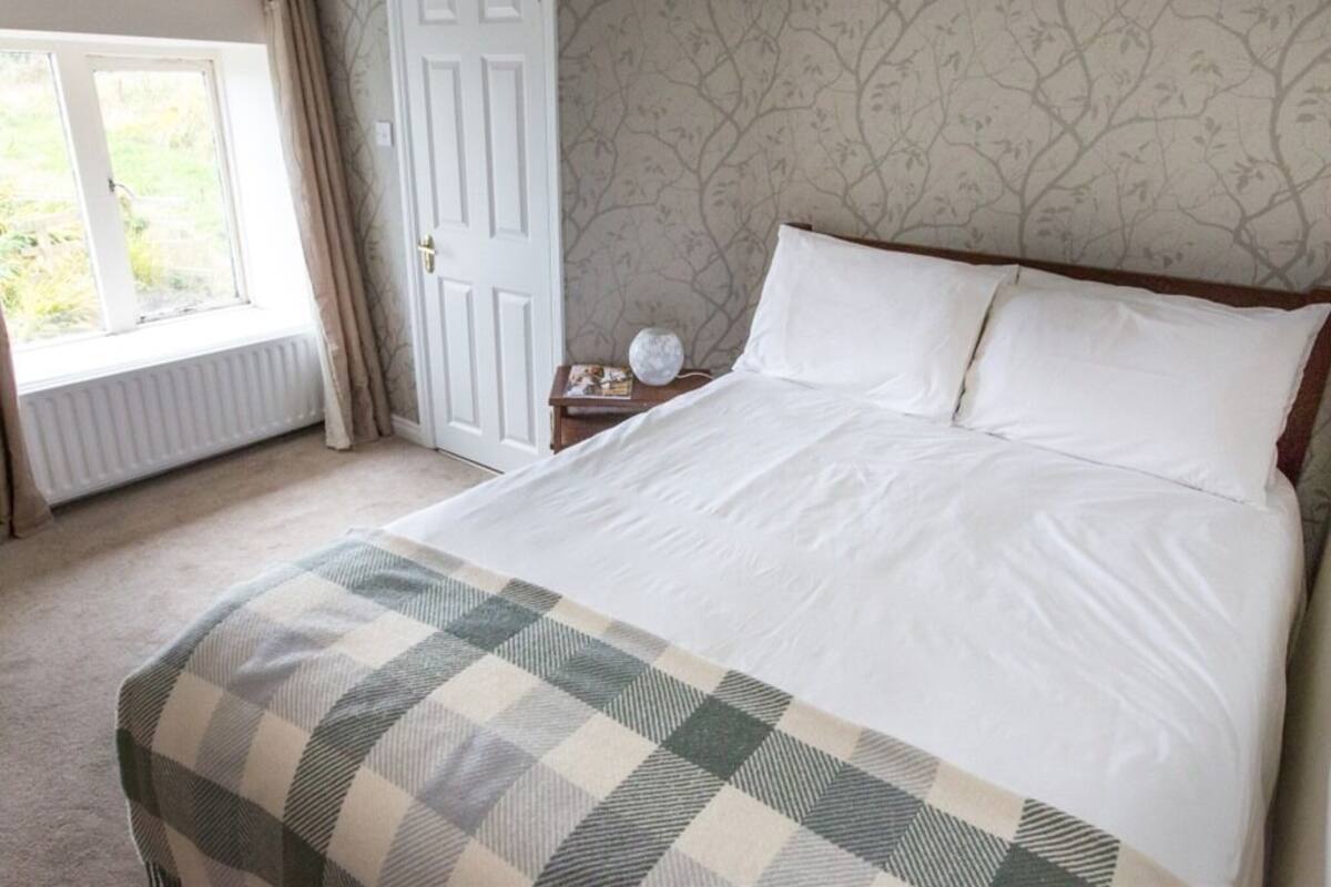 A bedroom with a large bed, a window with curtains, a radiator, and a patterned wallpaper.