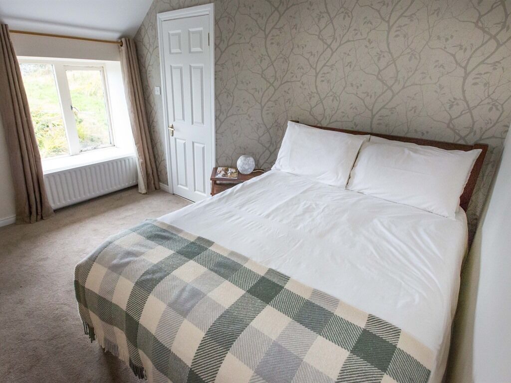 Une chambre à coucher avec un lit, une table de chevet, une fenêtre avec des rideaux et un radiateur.