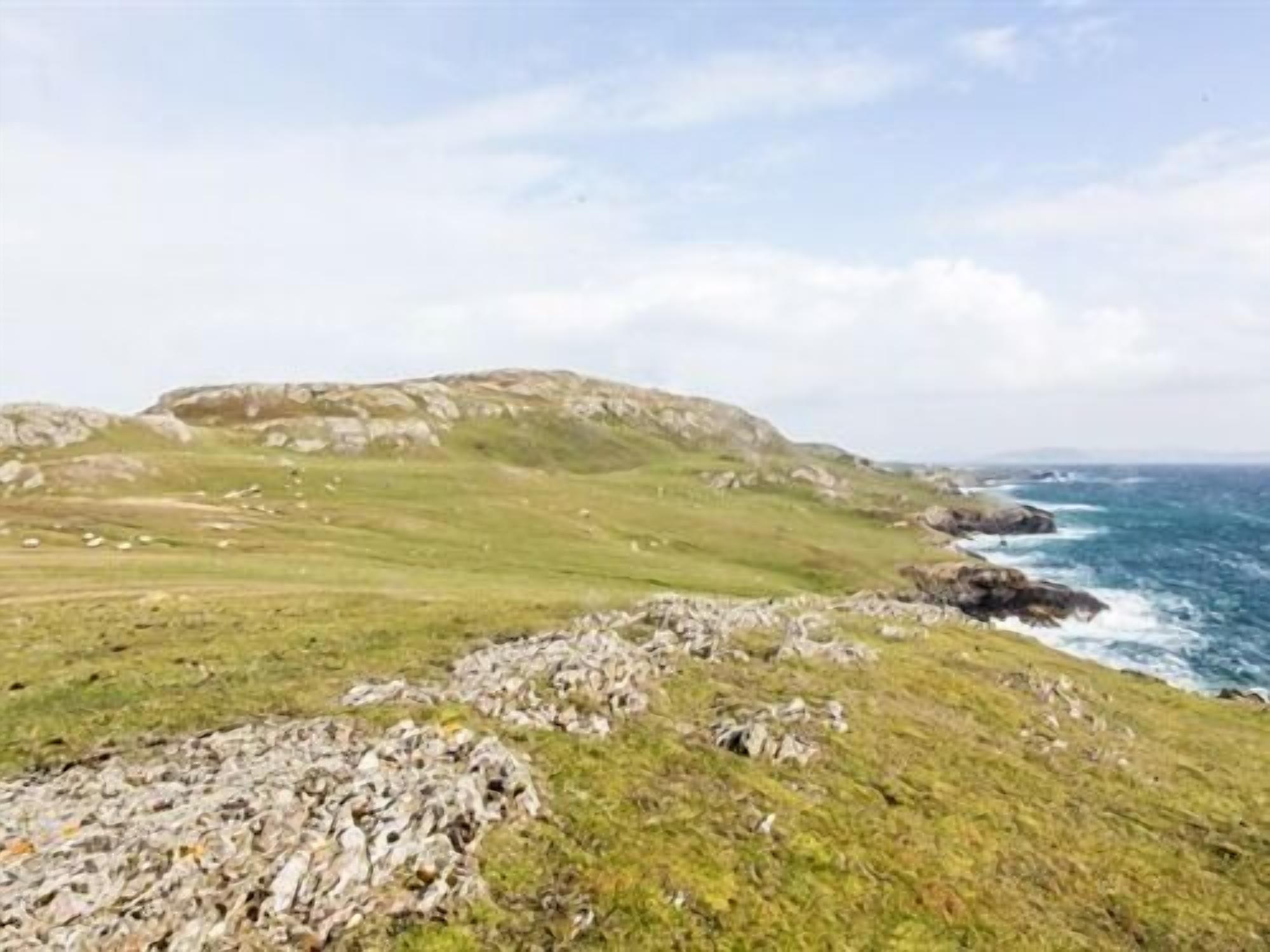 A coastal landscape with grassy terrain and rocky outcrops.