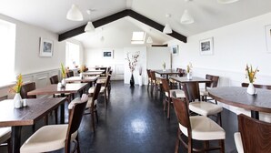 A spacious dining area with multiple tables and chairs, white pendant lights, and framed artwork on the walls. - The Beach Day's Bar & B&B (Inishbofin)