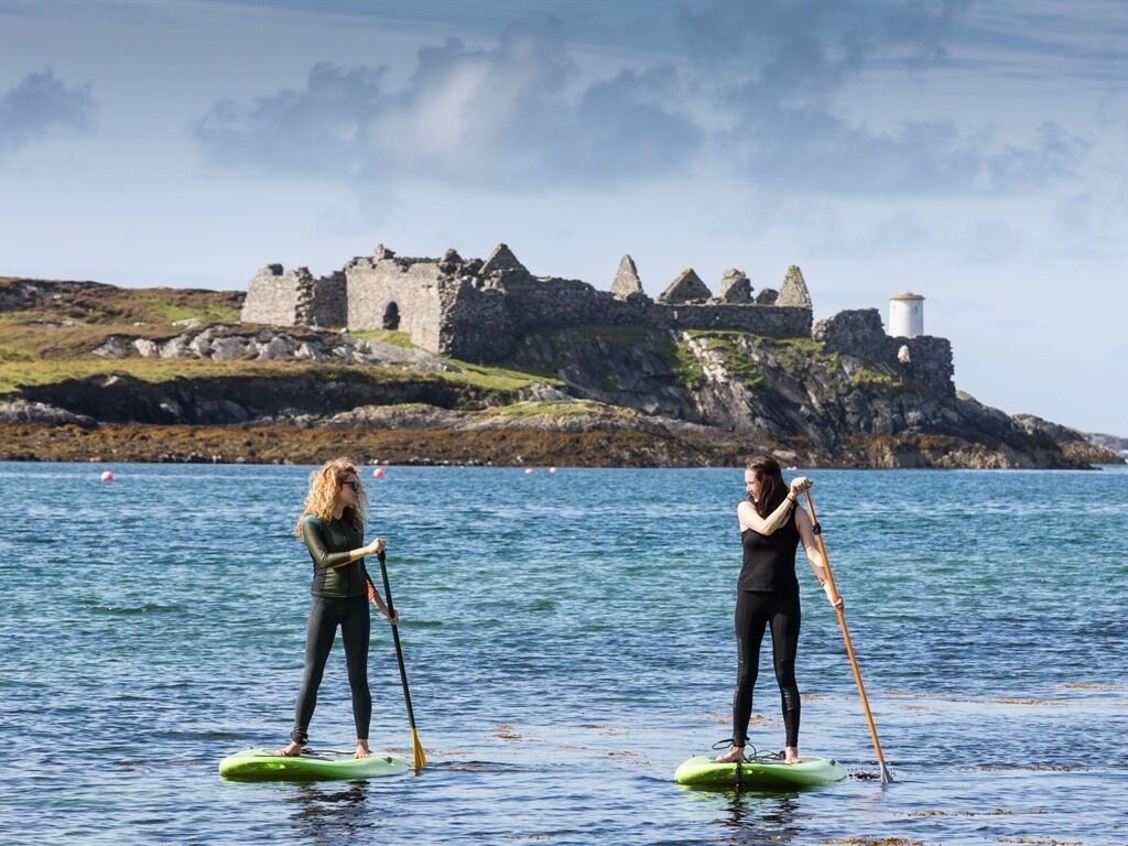 Dos personas haciendo paddleboard sobre aguas tranquilas, con un castillo histórico al fondo.
