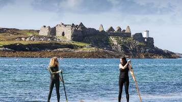 Dos personas haciendo paddleboard sobre aguas tranquilas, con un castillo histórico al fondo.