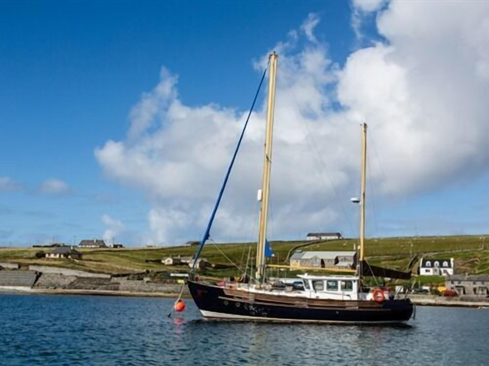 A boat docked at a harbor with a clear sky and grassy hills in the background.