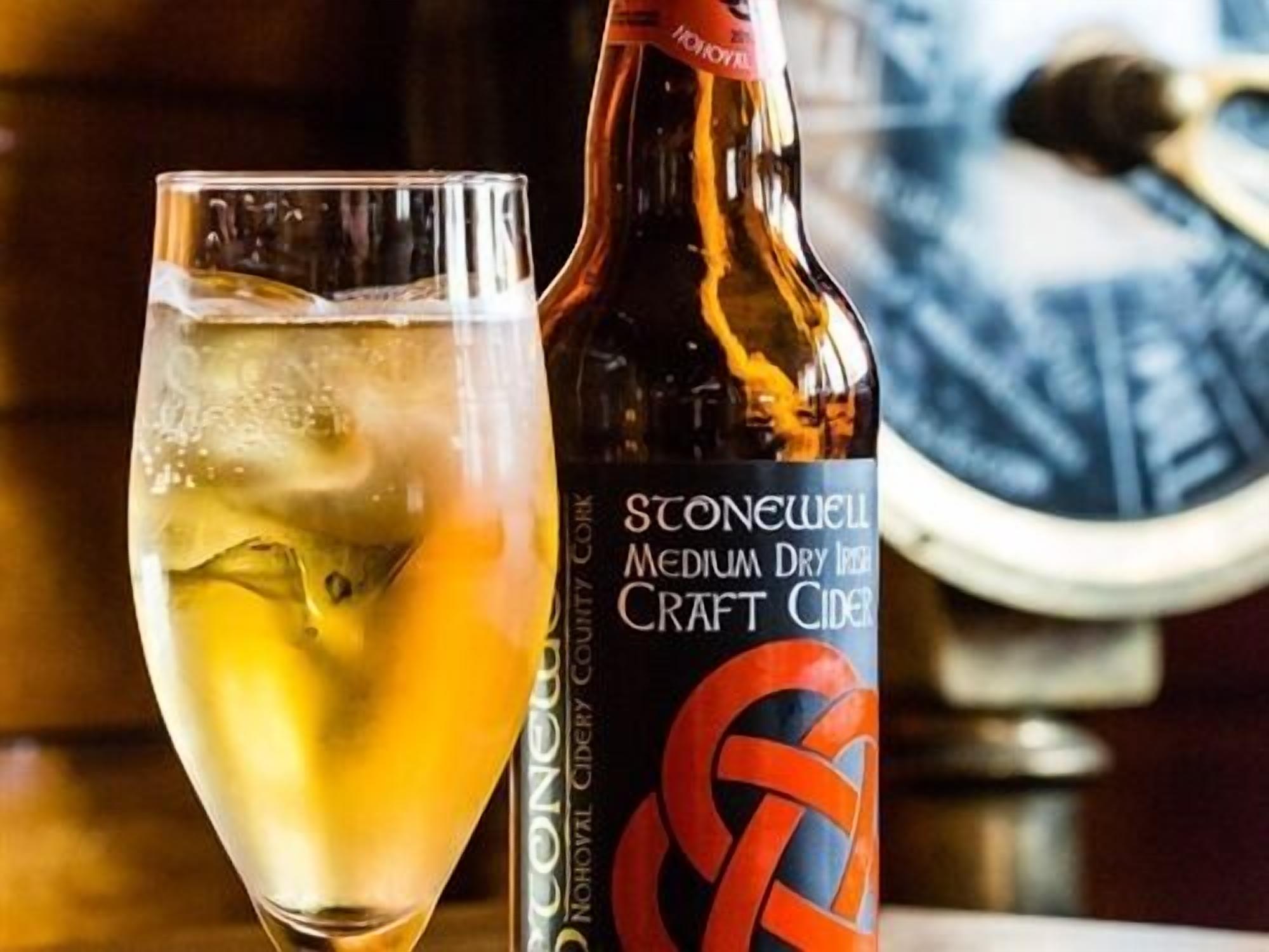 Une bouteille de cidre artisanal irlandais Stonewell, de type « Medium Dry », et un verre rempli de glaçons et garni d’une tranche d’orange.
