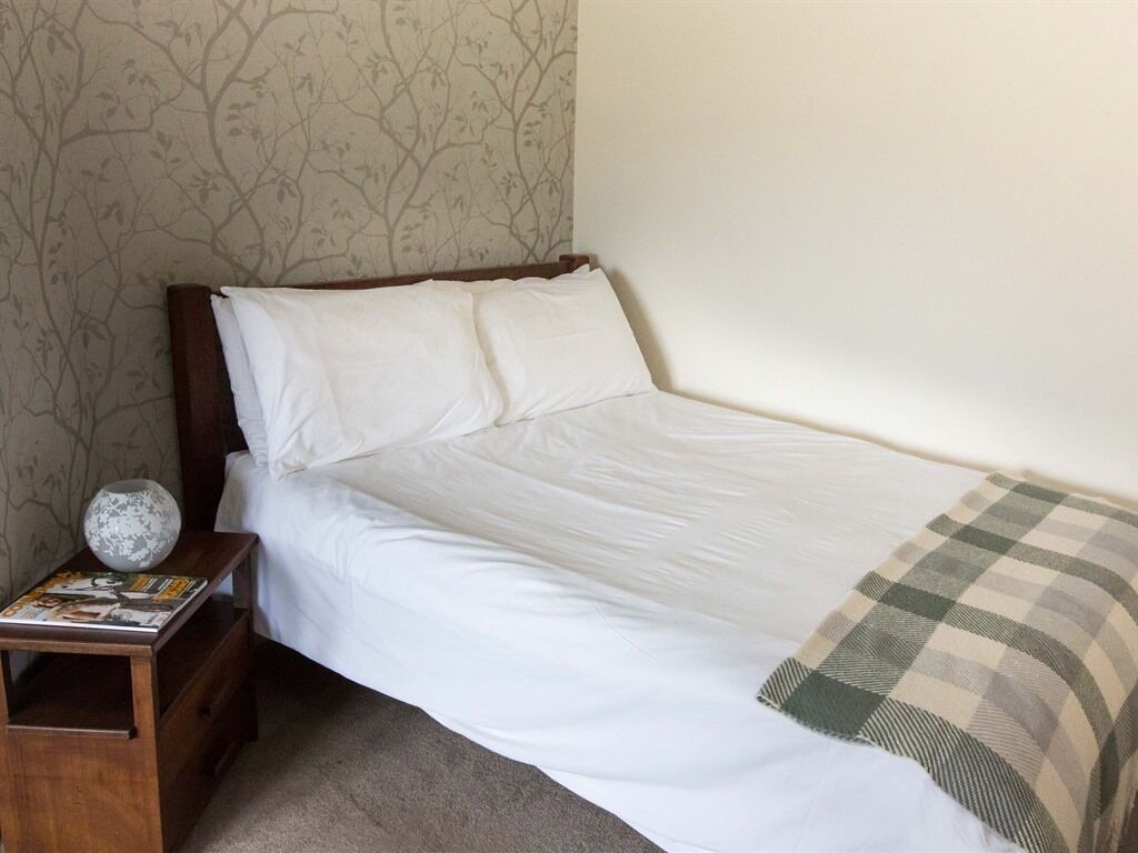 Ein Einzelbett mit weißen Bettwäsche, einem hölzernen Kopfteil und einer karierten Decke.
