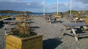 A coastal area with picnic tables and a flagpole. - The Beach Day's Bar & B&B (Inishbofin)