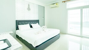 Une chambre d’hôtel moderne avec un grand lit, du linge de lit blanc, un mur décoratif au motif de briques, un lustre et une grande fenêtre offrant une belle vue.