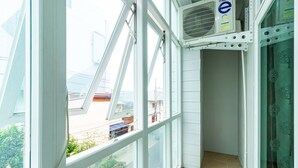 Une chambre d’angle avec de grandes fenêtres, un ventilateur de plafond et une vue sur la rue.