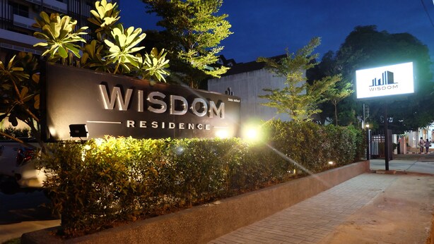 A nighttime view of a residential complex named 'Wisdom Residence' with illuminated signage and landscaped greenery. - Wisdom Residence (Hat Yai)