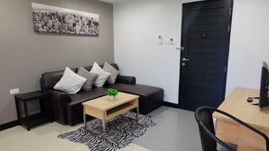 A modern living room with a dark brown sofa, a wooden coffee table, a zebra-patterned rug, a cityscape artwork on the wall, and a black door. - Wisdom Residence (Hat Yai)