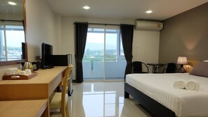 A hotel room with a bed, a desk, a chair, a television, a coffee maker, and a view of the outdoors. - Wisdom Residence (Hat Yai)