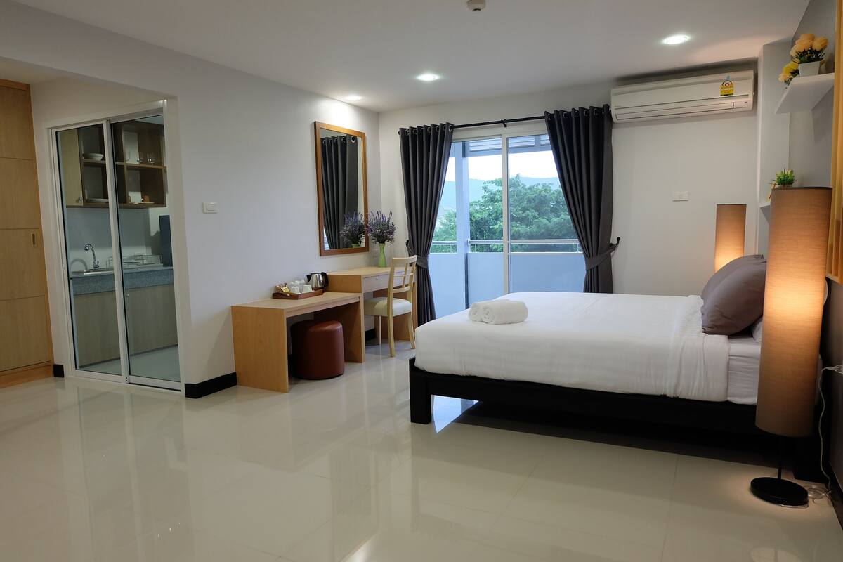 A modern hotel room with a bed, desk, and a view of the outdoors.
