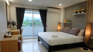 A hotel room with a bed, a desk, a chair, a window with curtains, an air conditioning unit, and a balcony with a view. - Wisdom Residence (Hat Yai)