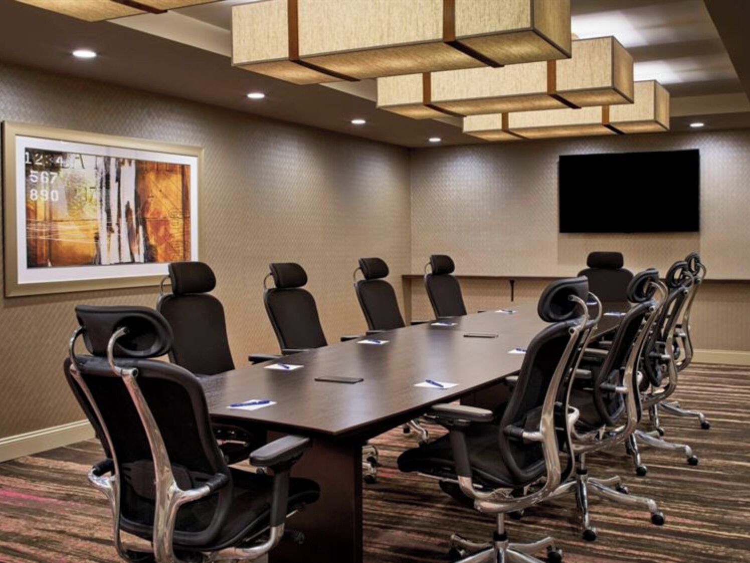 A conference room with a long table, multiple chairs, a projector screen, and a framed artwork on the wall.