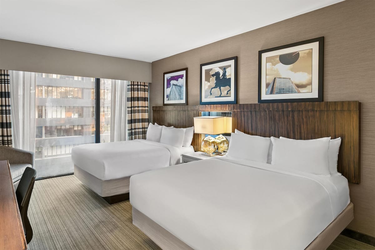 A hotel room with two beds, a desk, and a chair. There are three framed pictures on the wall.
