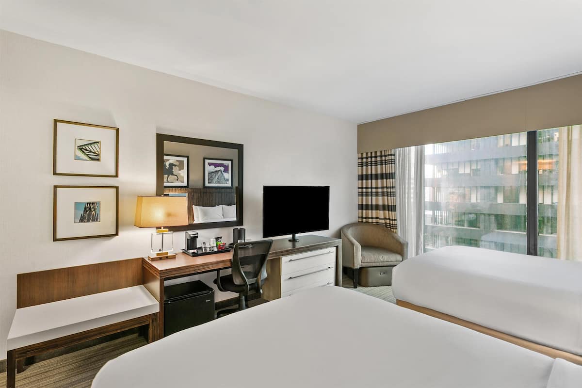A hotel room with a bed, desk, chair, TV, and large windows.