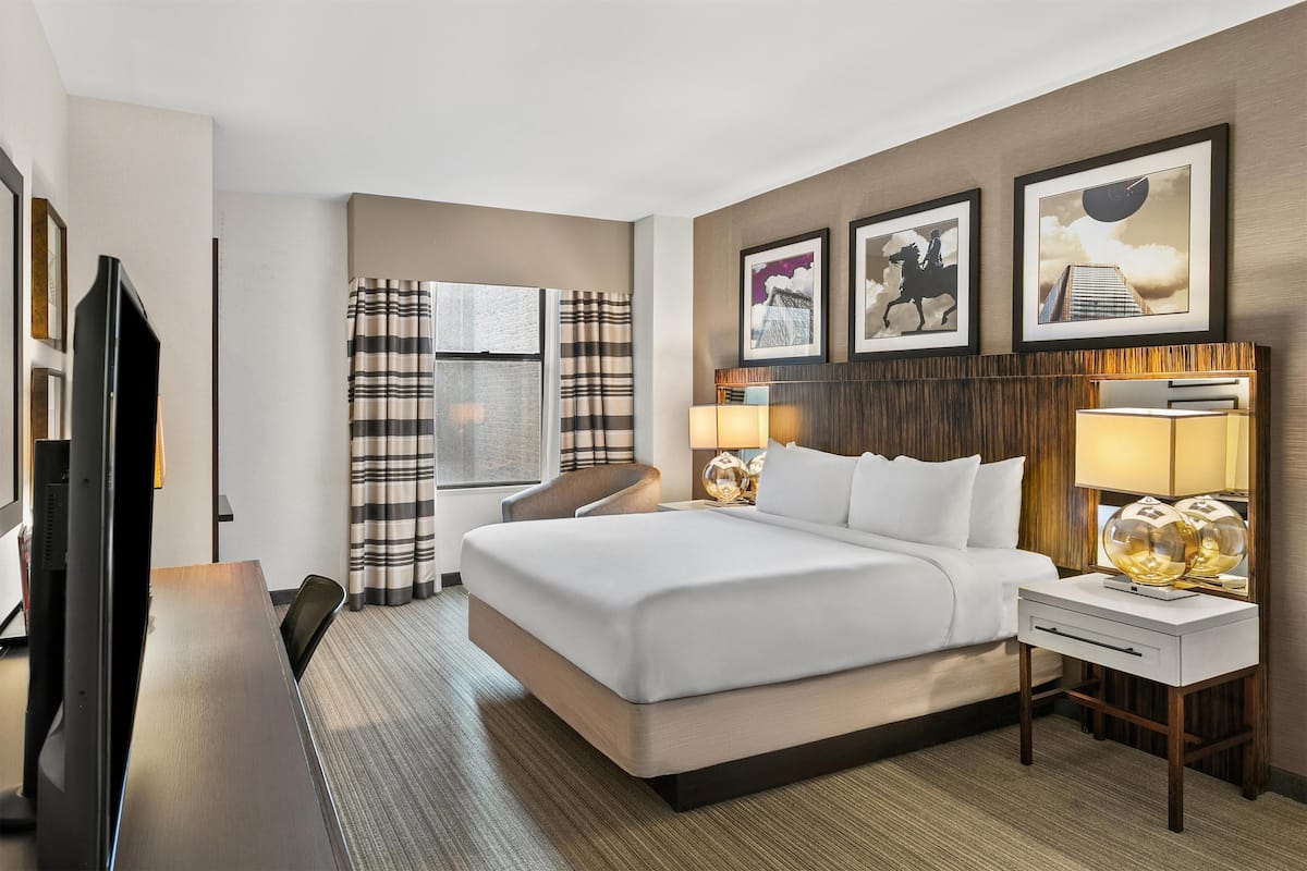 A hotel room with a large bed, a desk, a TV, and a window with curtains.