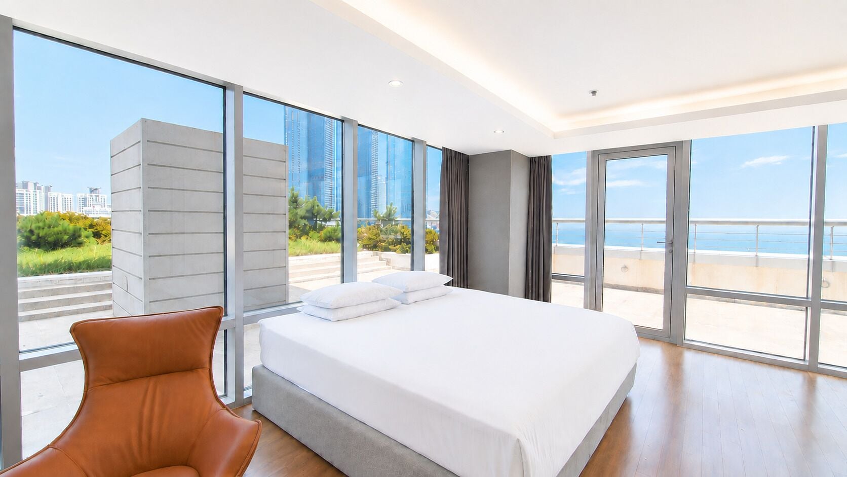 A modern hotel room with a large bed, a seating area, and a view of the sea.
