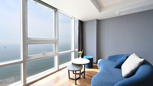 En moderne stue med et stort vindue, en blå sofa, et lille rundt bord og en blå skammel.